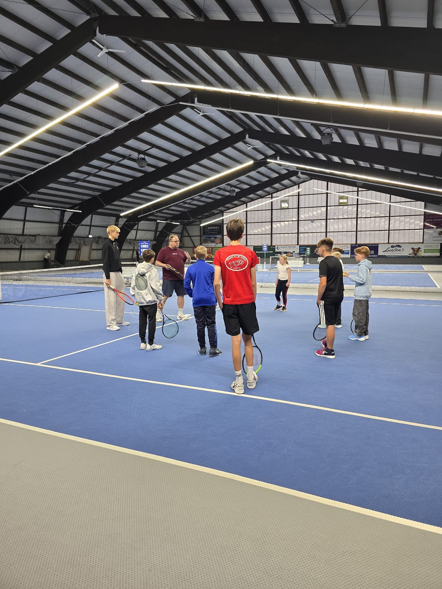 Kinder und Jugendliche des Tennis-Club Oyten stehen mit Tennisschlägern in der Tennishalle zusammen und nehmen an einer praktischen Übung des „Mental Match Winner“-Programms mit Mentaltrainer Marc Nienstedt teil.